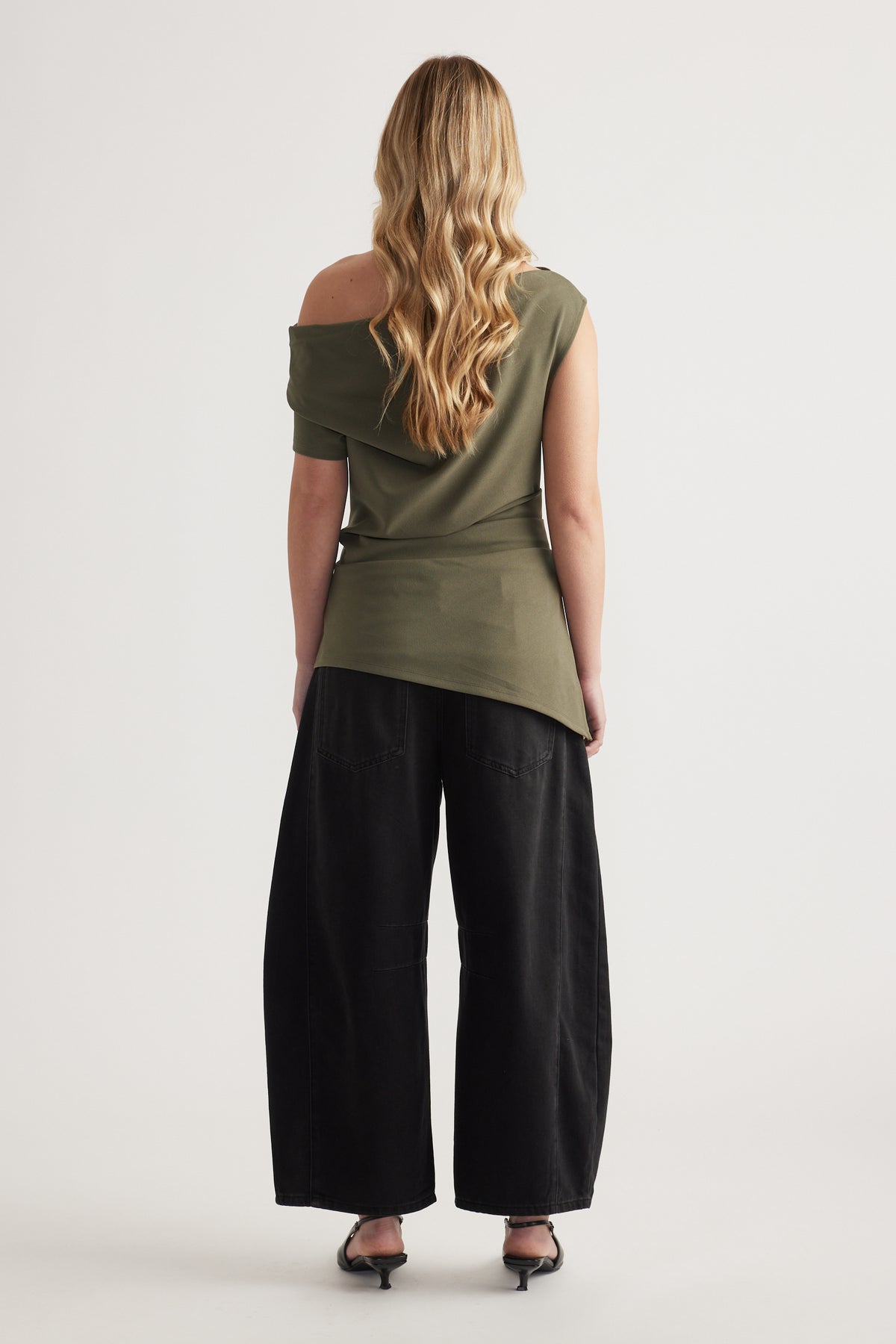 Woman wearing an olive asymmetric off shoulder top with black wide leg pants and heels