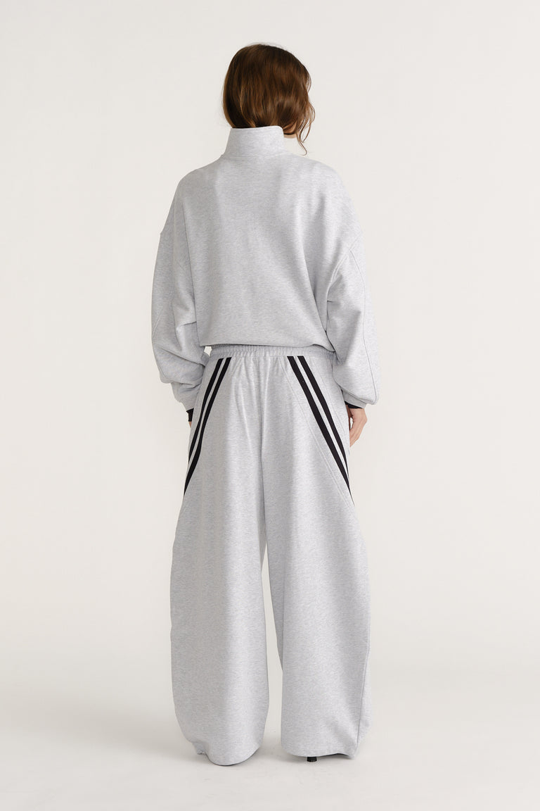 Woman seen from behind in light grey wide-leg trackpants with black stripe details and a matching high-neck sweatshirt