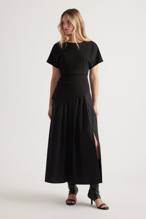 Woman wearing a black midi dress with short sleeves and a side slit, styled with heeled open-toe boots