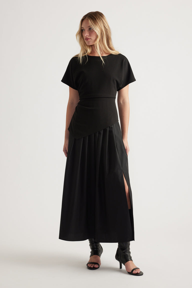 Woman wearing a black midi dress with short sleeves and a side slit, styled with heeled open-toe boots