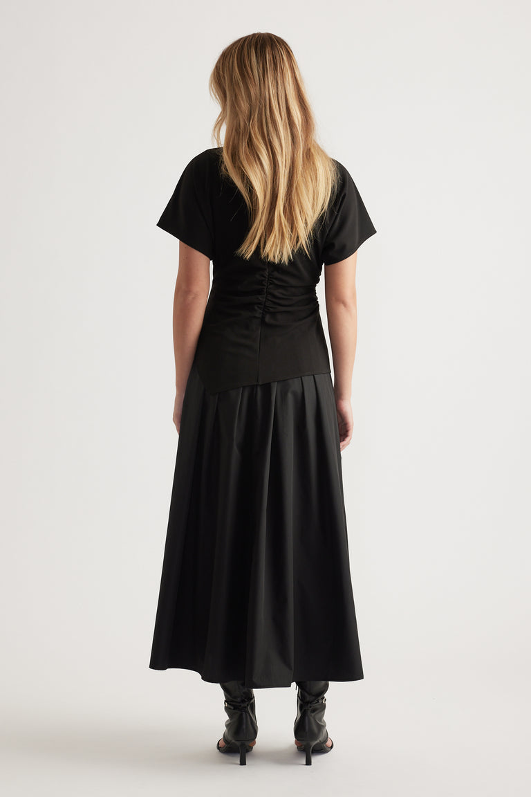 Back view of woman wearing a black spliced midi dress with short sleeves and relaxed silhouette, styled with black heeled boots