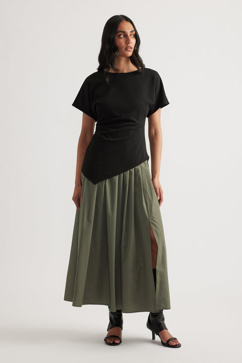 Woman wearing a black and olive spliced midi dress with short sleeves, round neck and pleated A-line skirt