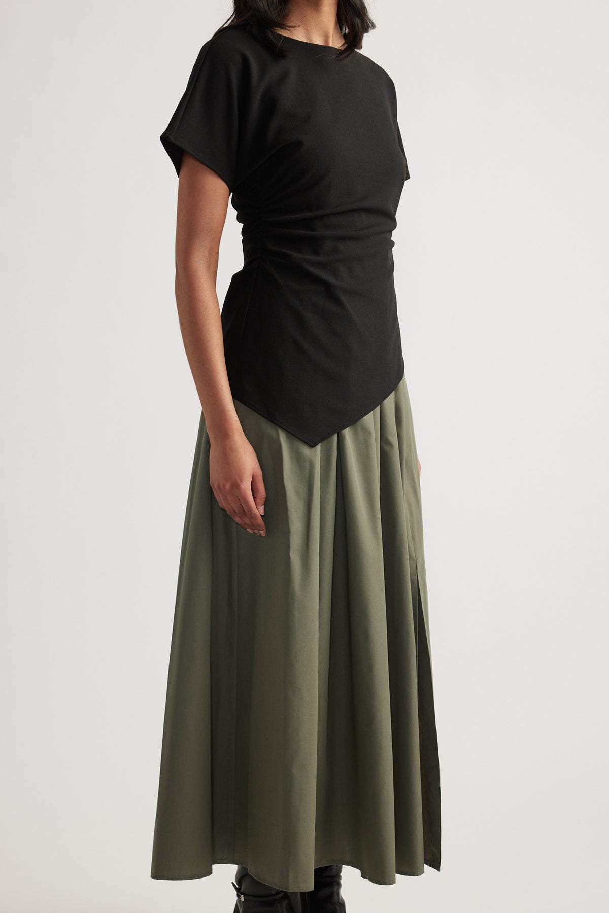 Woman wearing a black short sleeve spliced midi dress with gathered waist and pleated olive green A-line skirt