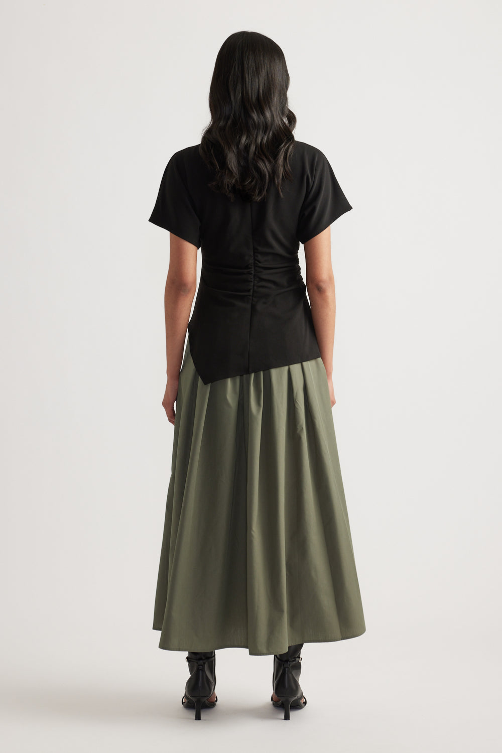 Back view of woman wearing a black and olive spliced midi dress with short sleeves and pleated A-line skirt