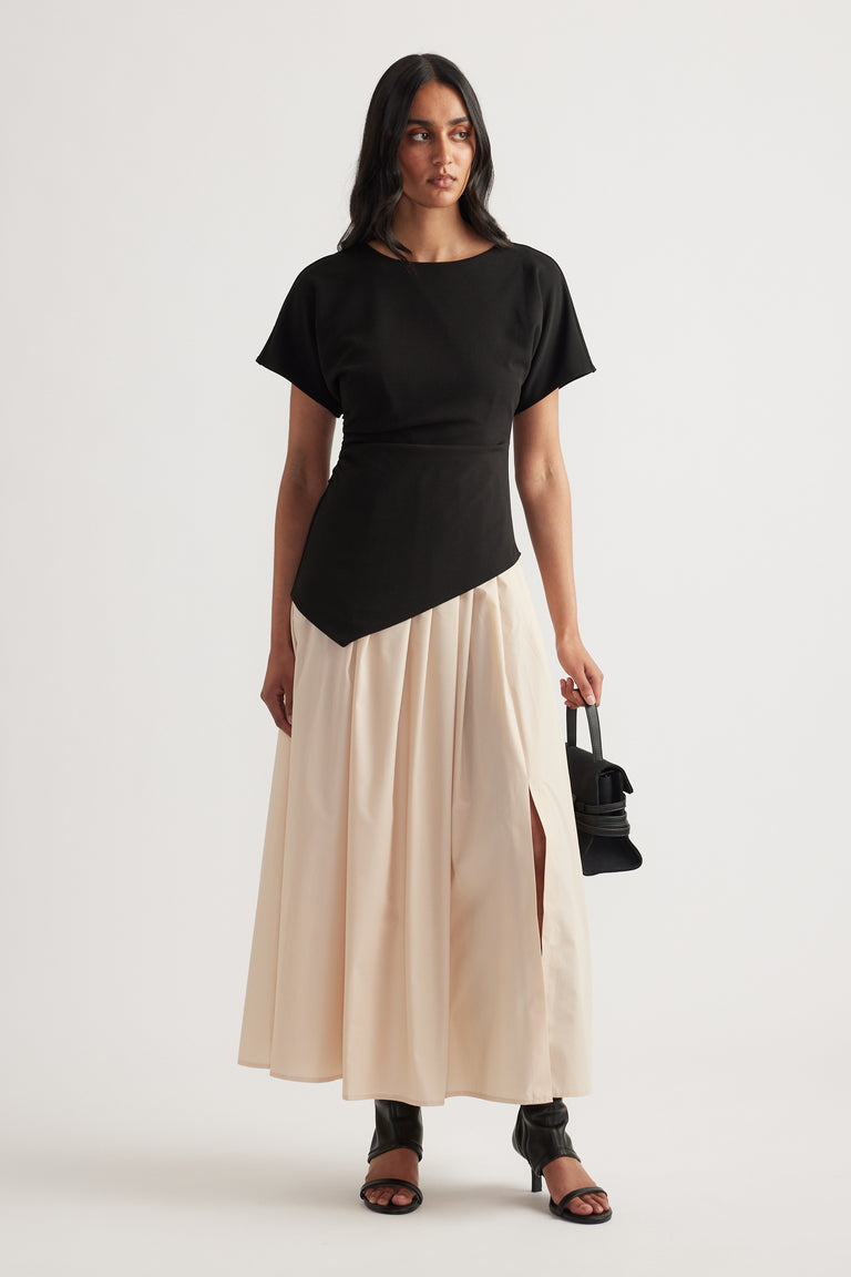 Woman wearing a black and cream spliced pleated midi dress with short sleeves and black sandals