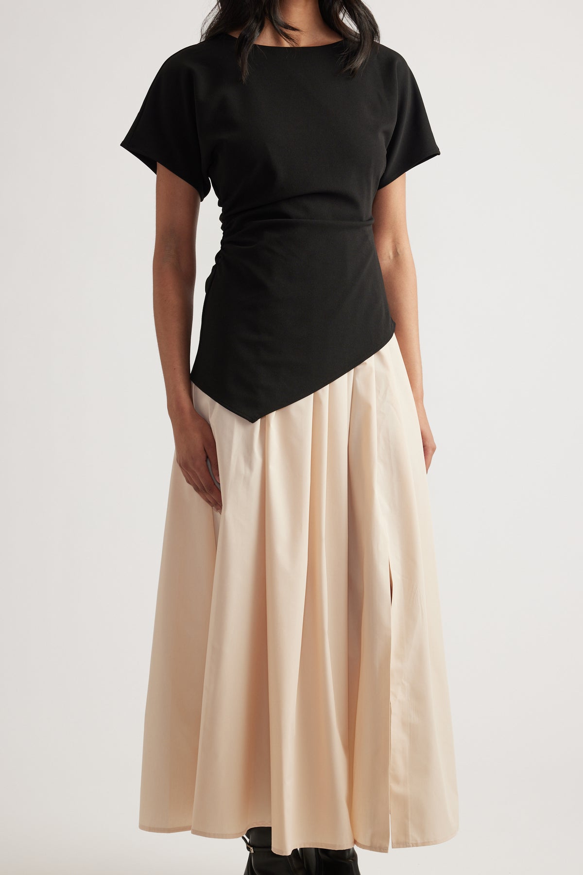 Woman wearing a black short sleeve dress with a pleated cream midi skirt and asymmetric hem