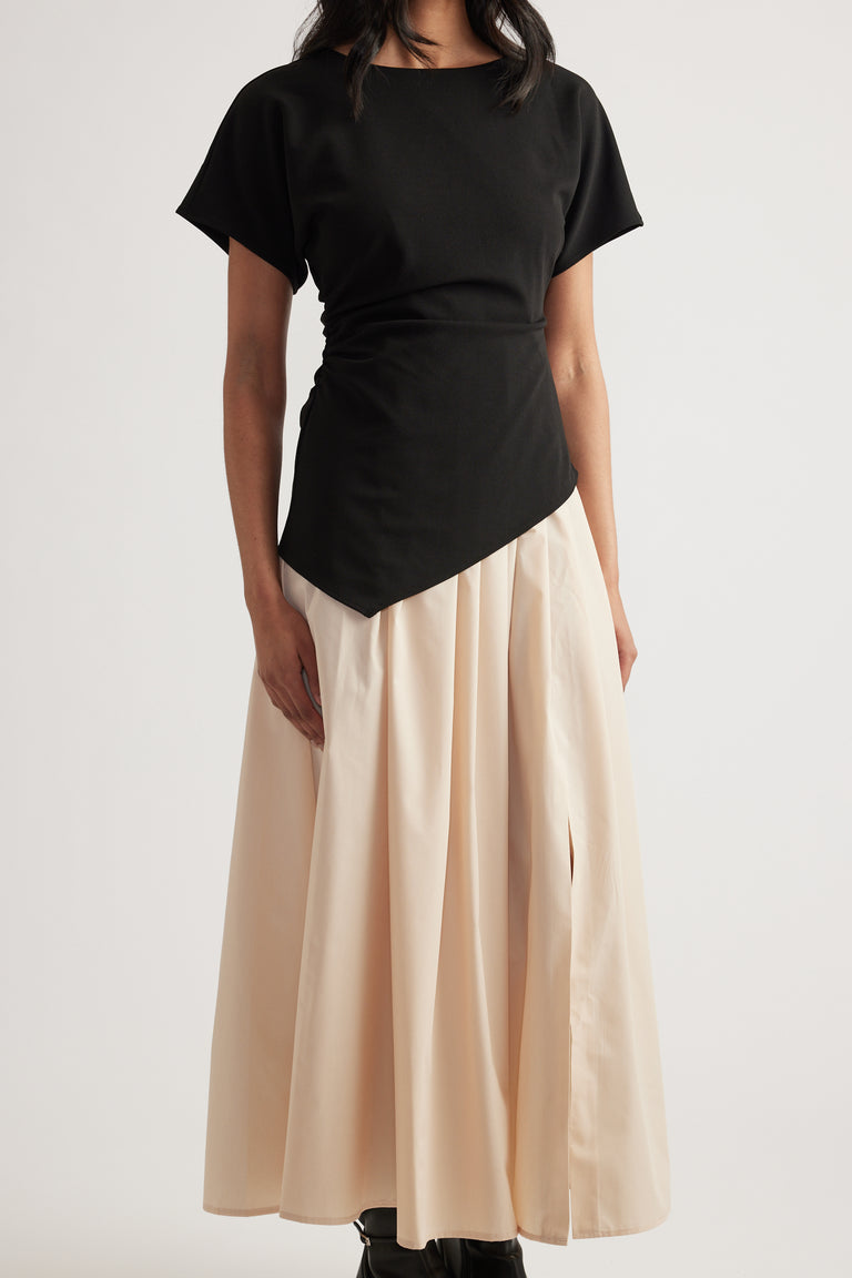 Woman wearing a black short sleeve dress with a pleated cream midi skirt and asymmetric hem