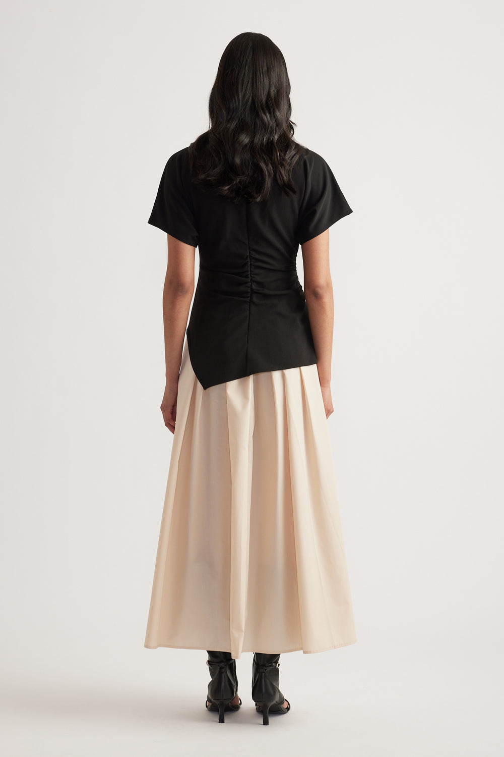 Woman viewed from behind wearing a black short sleeve midi dress with a pleated cream skirt and black boots
