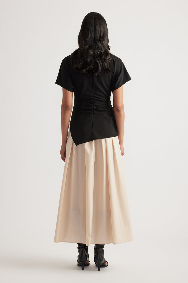 Woman viewed from behind wearing a black short sleeve midi dress with a pleated cream skirt and black boots