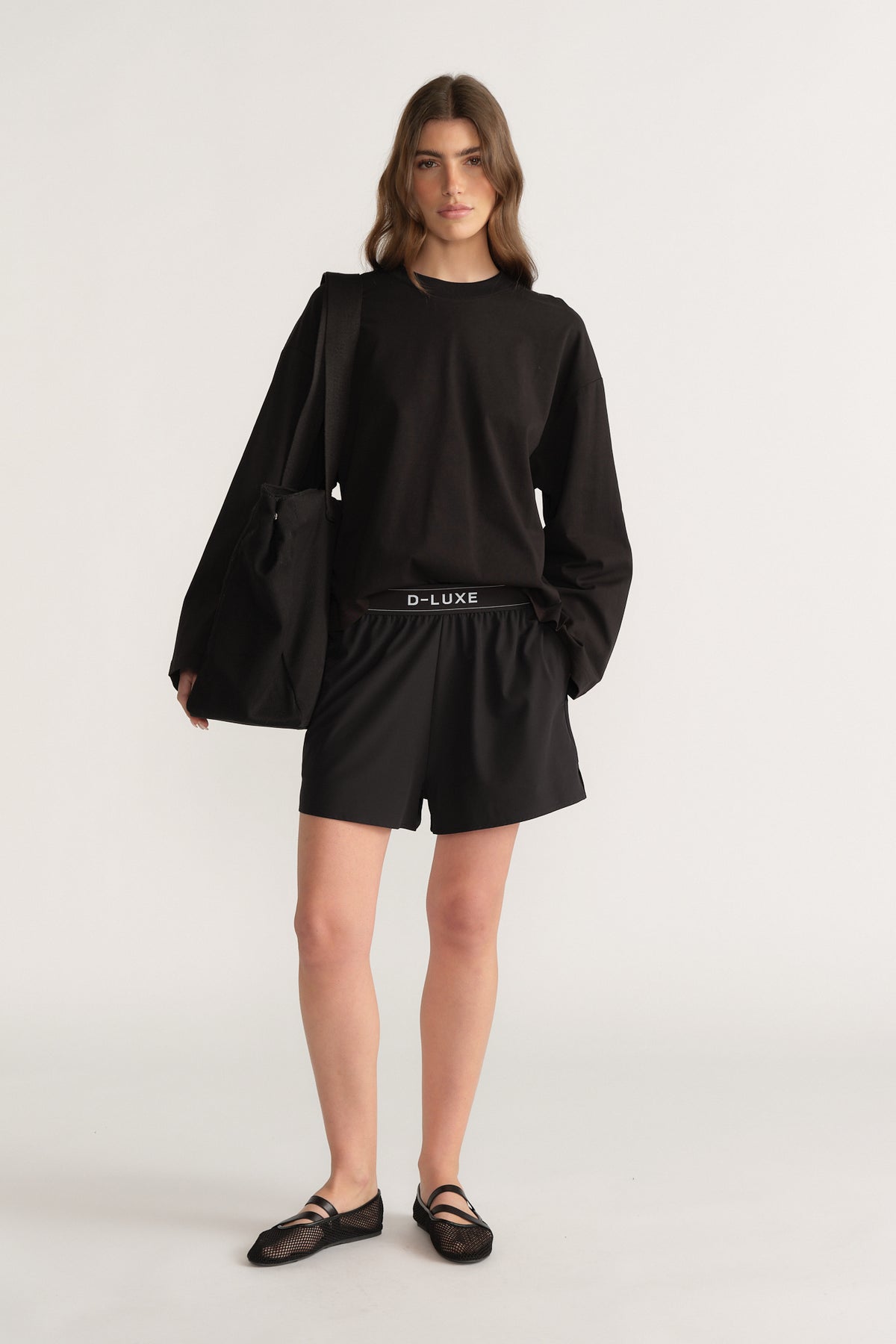 Model wearing black lightweight elastic waist shorts with a long sleeve top and shoulder bag