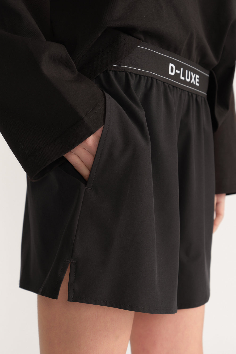 Close up of black D-Luxe shorts with an elastic waistband, side pockets and an above knee flare hem