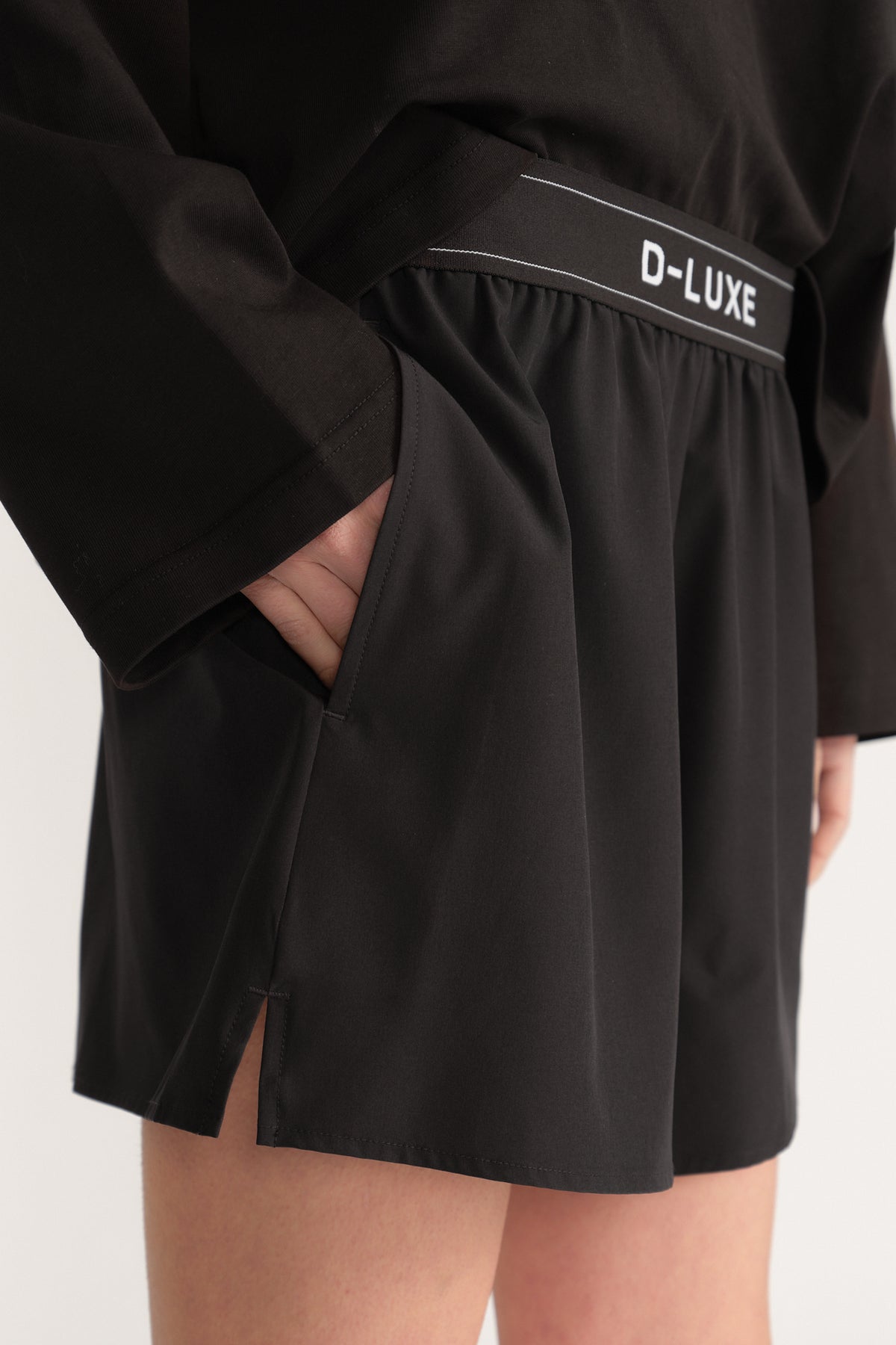 Close up of black D-Luxe shorts with an elastic waistband, side pockets and an above knee flare hem