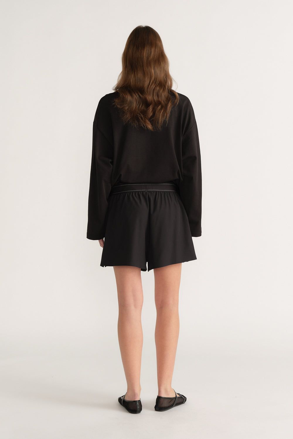 Woman wearing black elastic waist shorts with a black long sleeve top, shown from behind