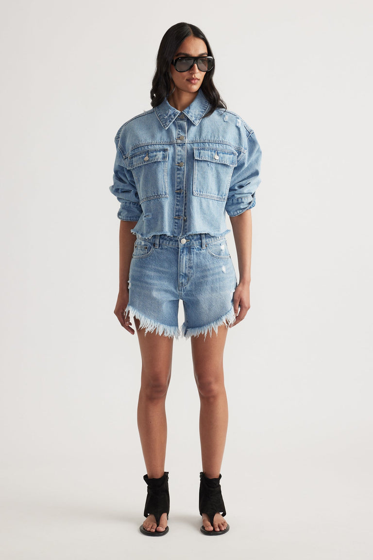 Woman wearing a cropped denim jacket paired with high rise, frayed hem distressed denim shorts and black open-toe heels