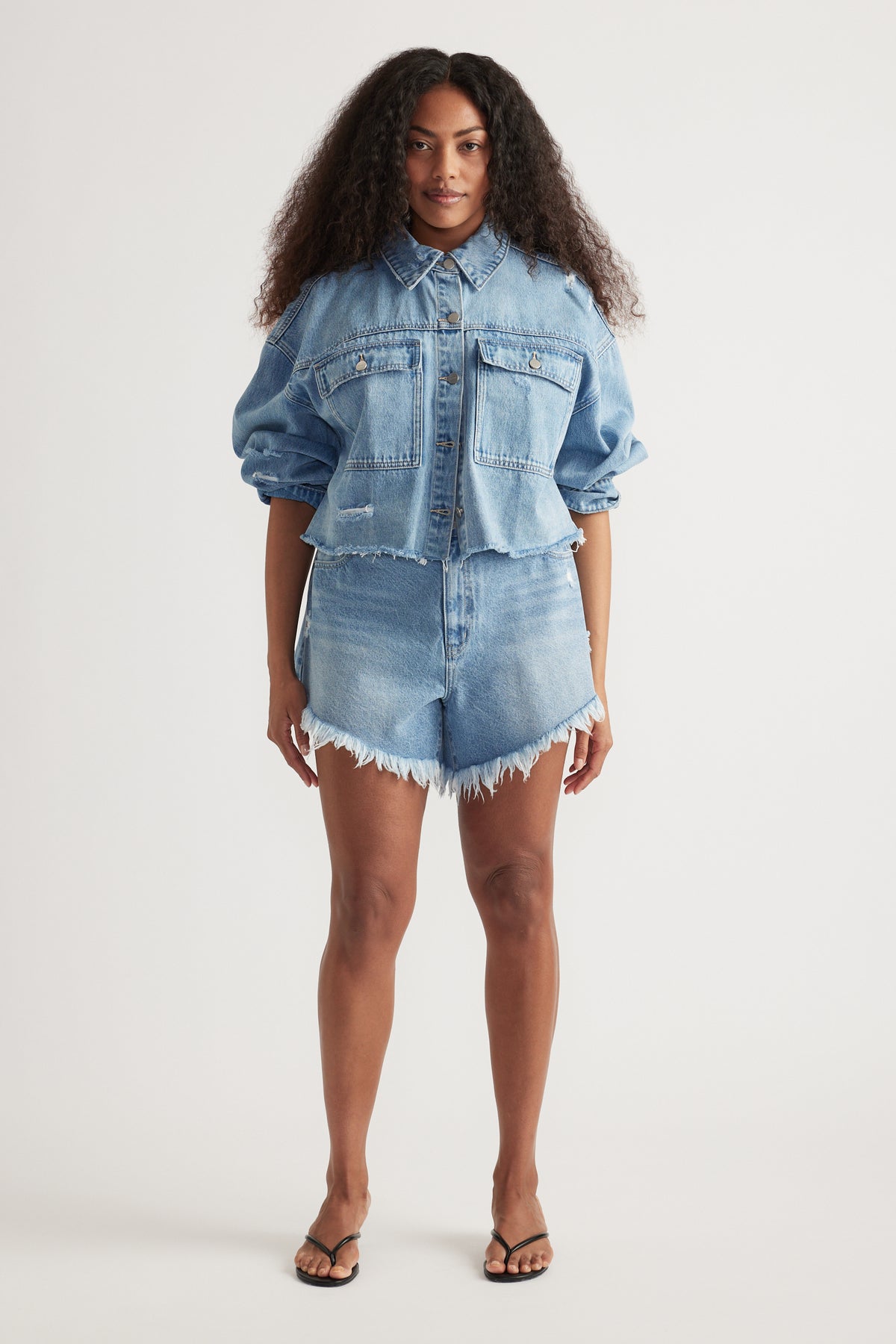 Woman wearing a relaxed fit cropped denim jacket with puffed sleeves paired with distressed high-waisted denim shorts