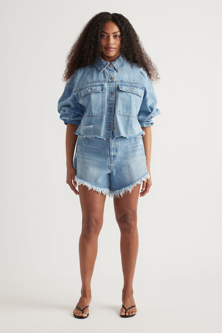Woman wearing a relaxed fit cropped denim jacket with puffed sleeves paired with distressed high-waisted denim shorts