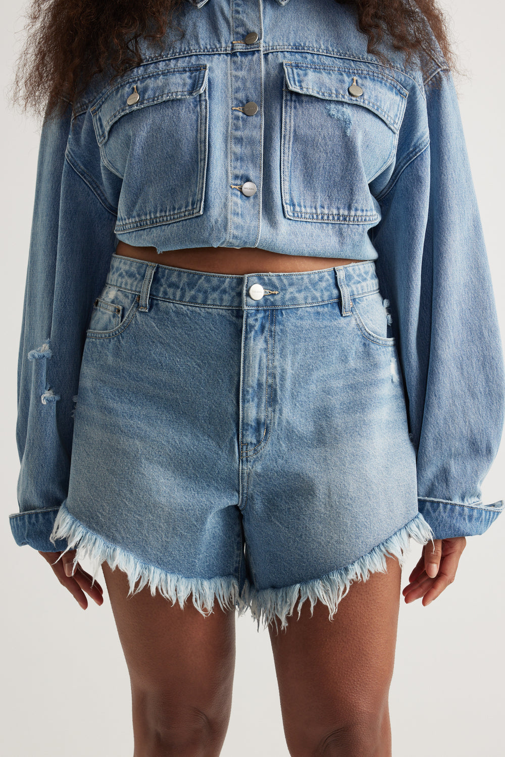Woman wearing high-waisted light blue denim shorts with frayed hem paired with cropped denim jacket