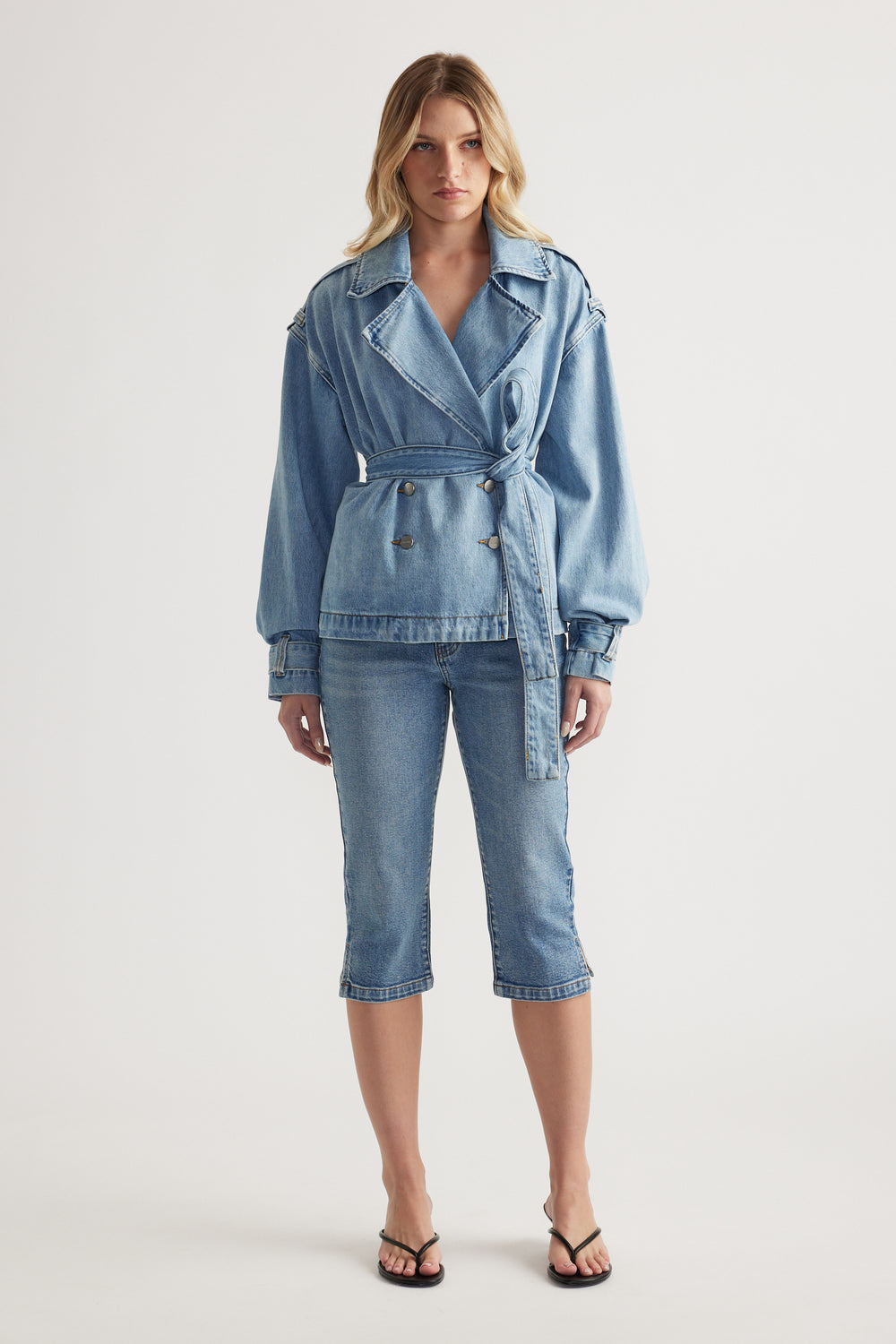 Woman wearing a belted denim jacket with cropped denim capri pants and strappy sandals