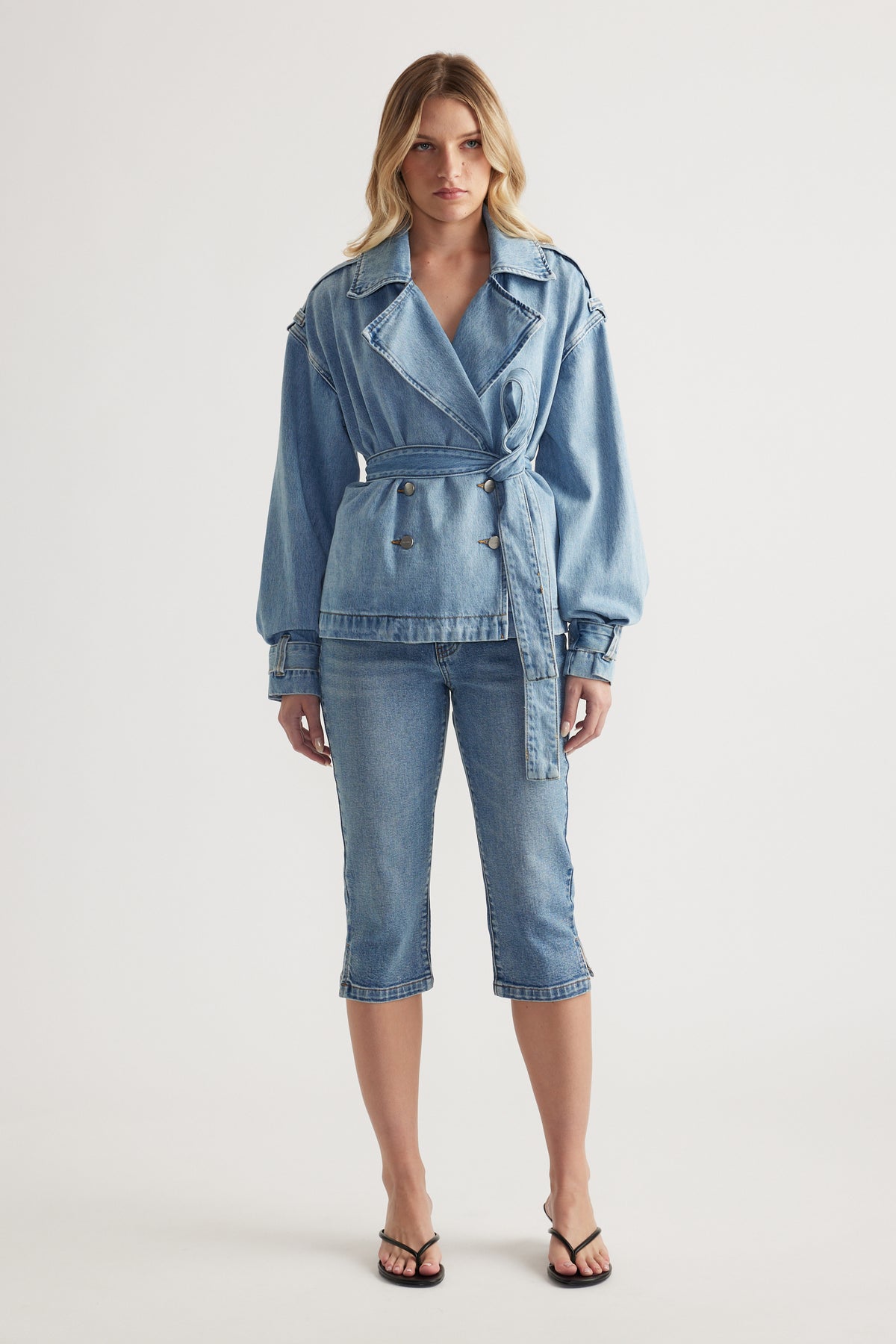 Woman wearing a belted denim jacket with cropped denim capri pants and strappy sandals