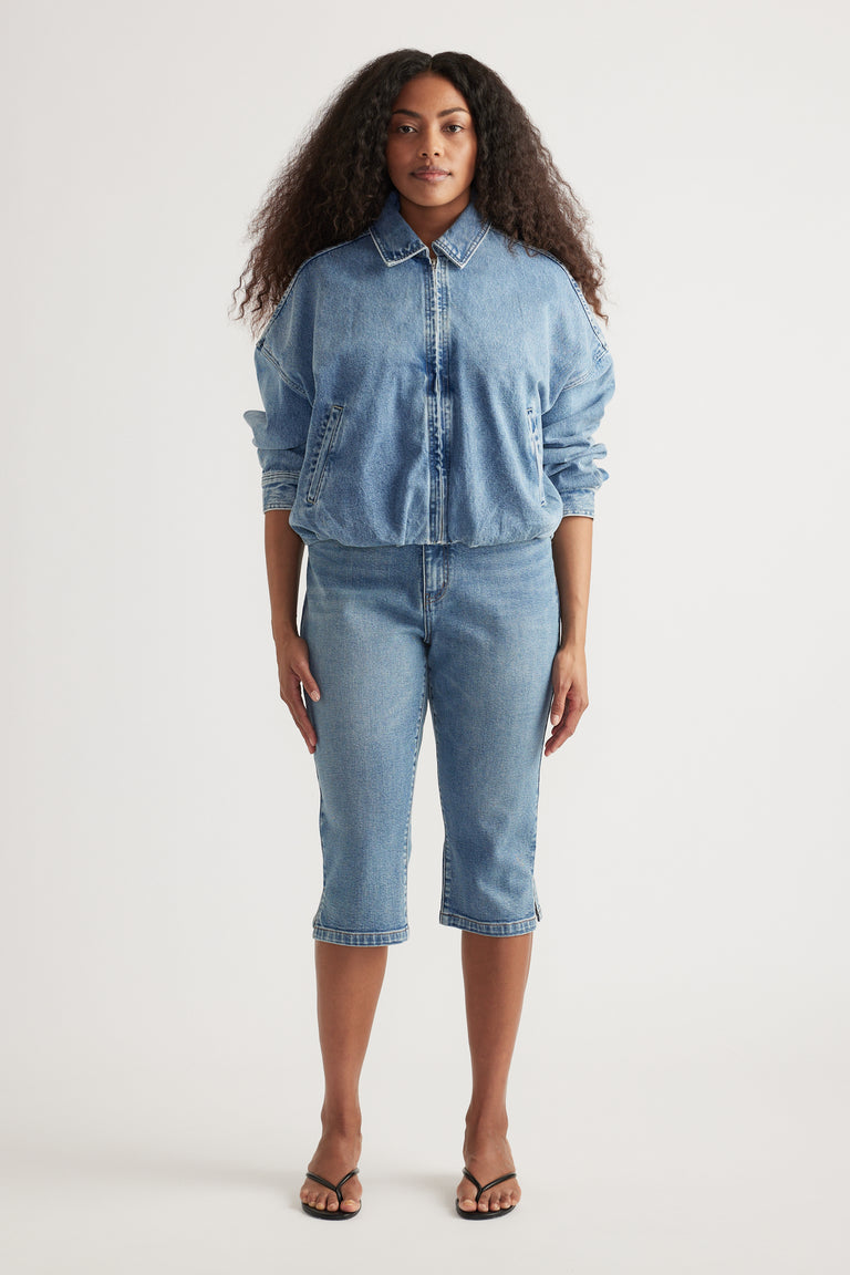 Woman wearing light wash high rise denim capri jeans with a matching button up denim shirt and sandals