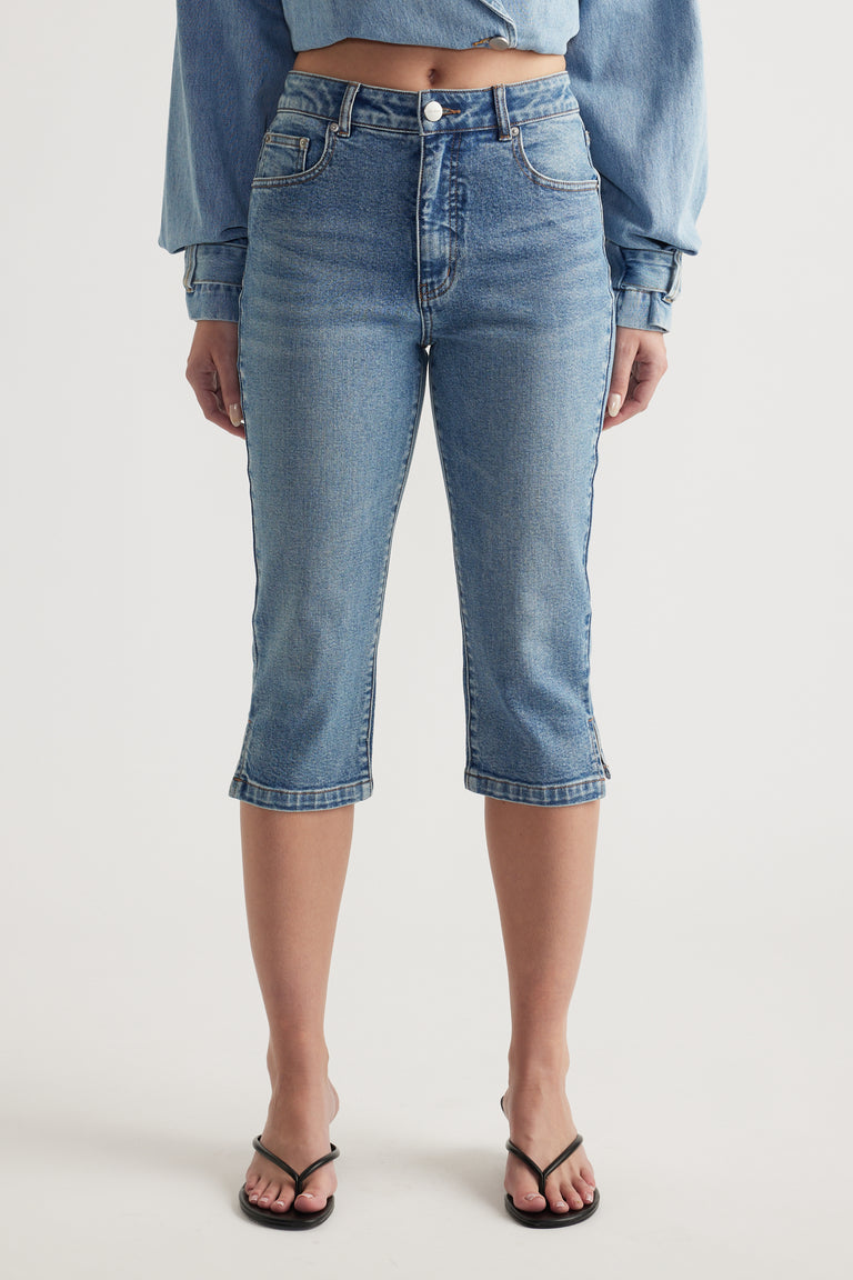 Woman wearing high rise blue denim capri pants with a cropped blue top and black sandals