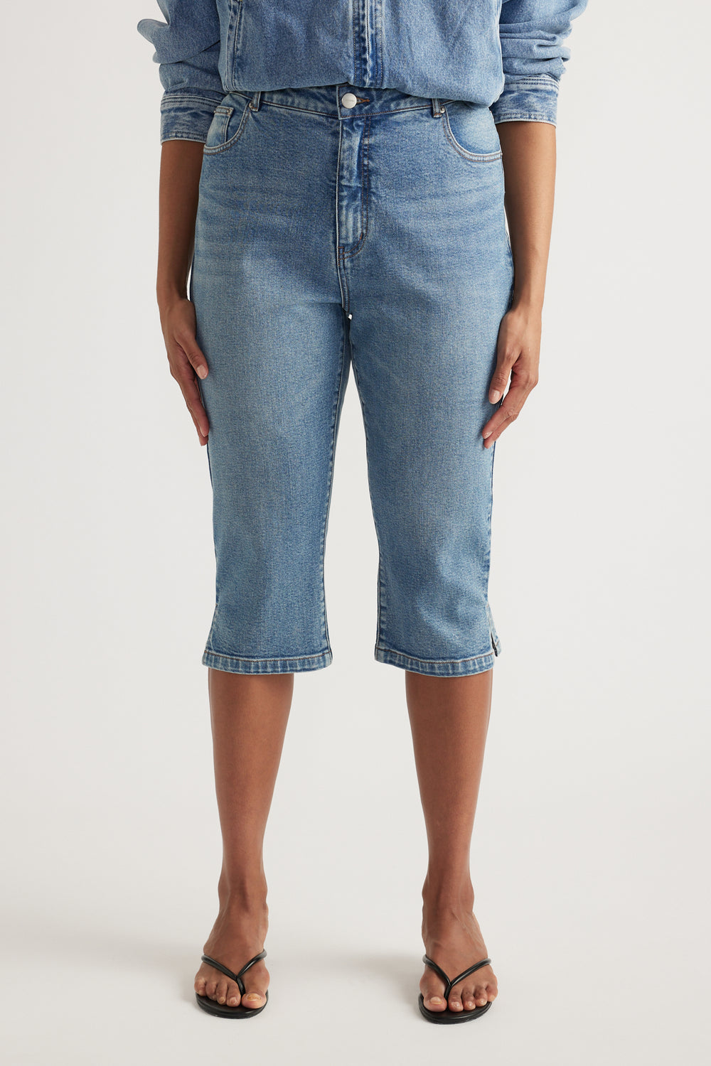 Woman wearing high-rise blue denim capris with a slim leg and black sandals