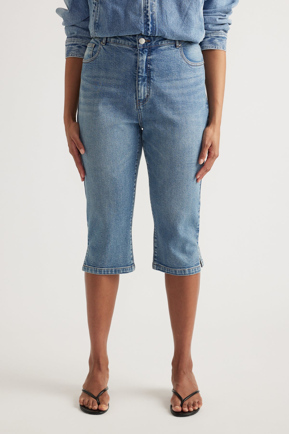 Woman wearing high-rise blue denim capris with a slim leg and black sandals