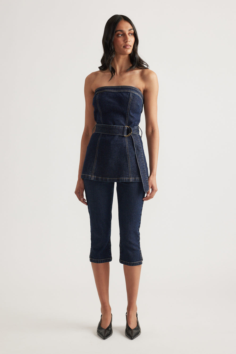 Woman wearing a strapless dark denim top with a belted waist and matching slim fit capri jeans