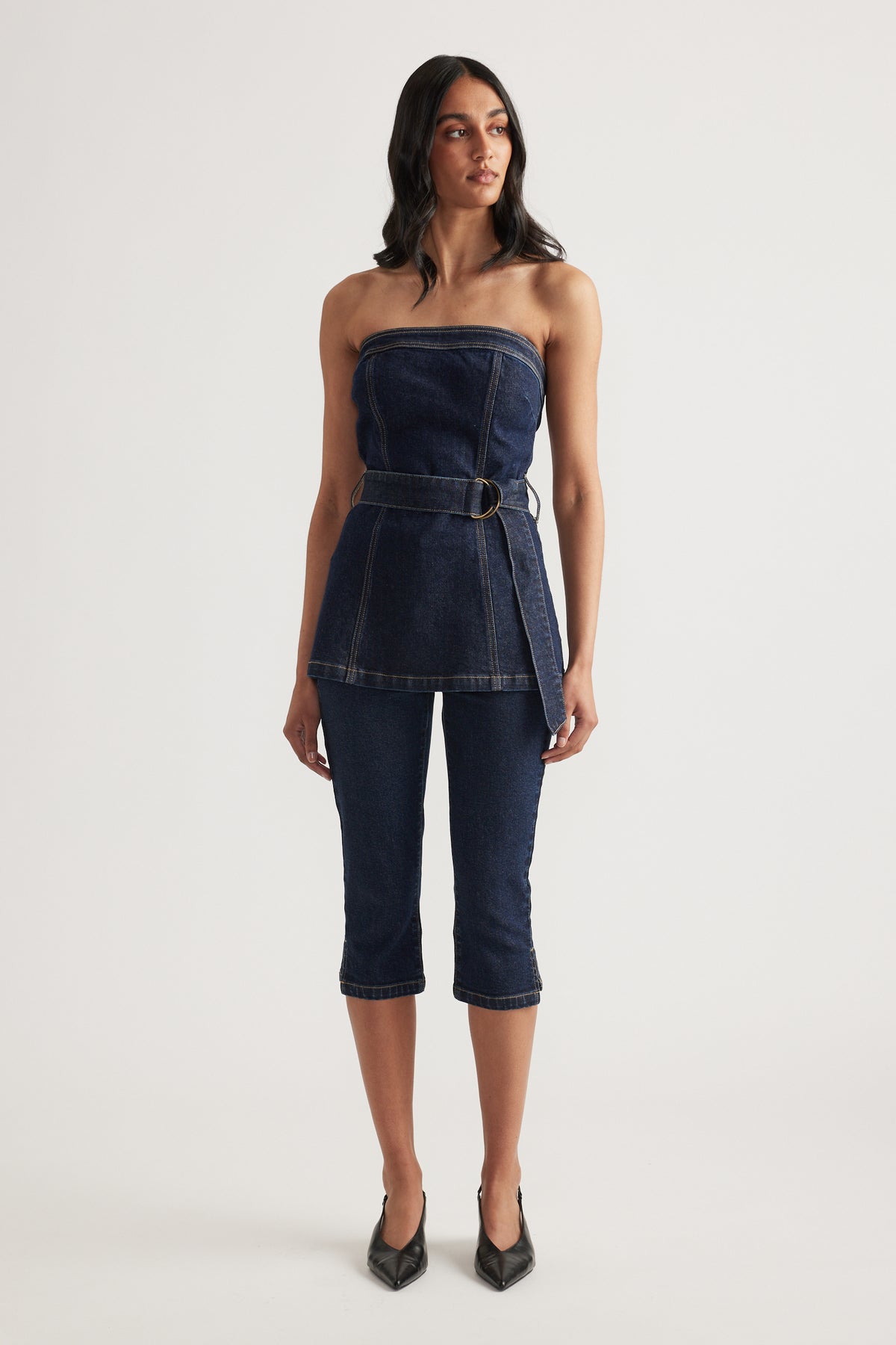 Woman wearing a strapless dark denim top with a belted waist and matching slim fit capri jeans