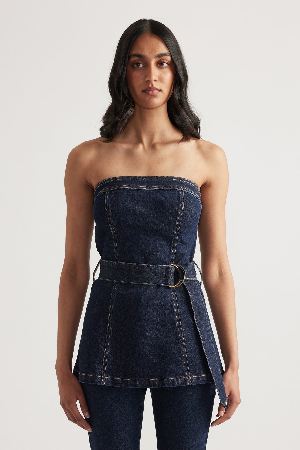 Woman wearing a dark denim strapless top with a belted waist and matching jeans