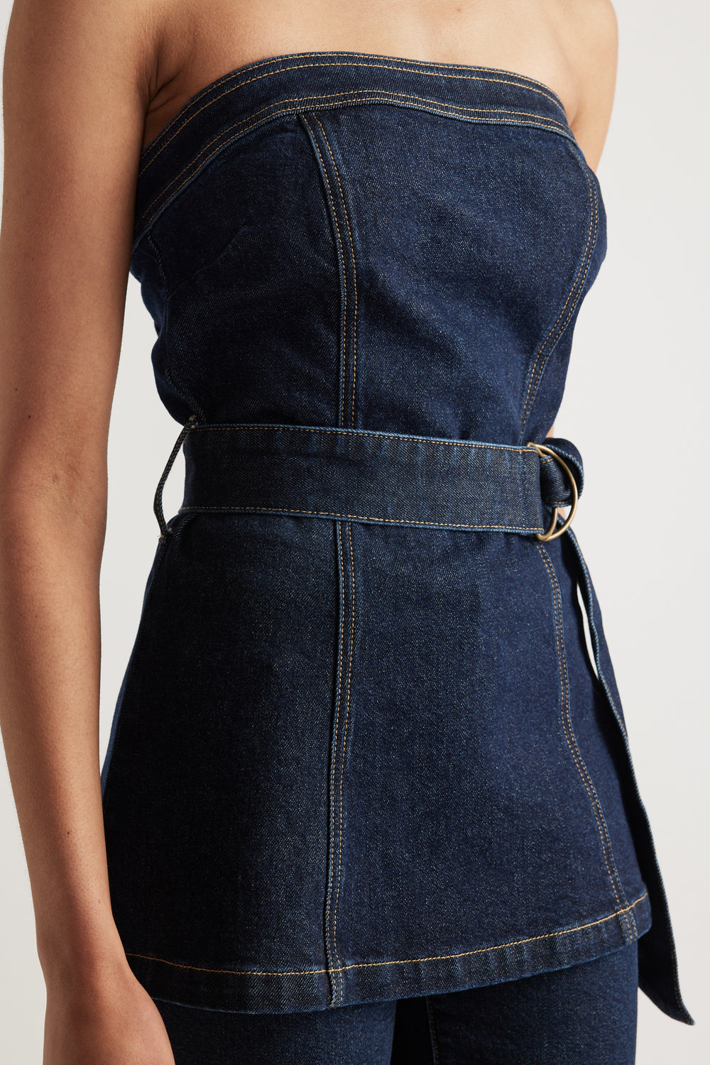 Model wearing a strapless dark denim top with a belted waist and longline silhouette