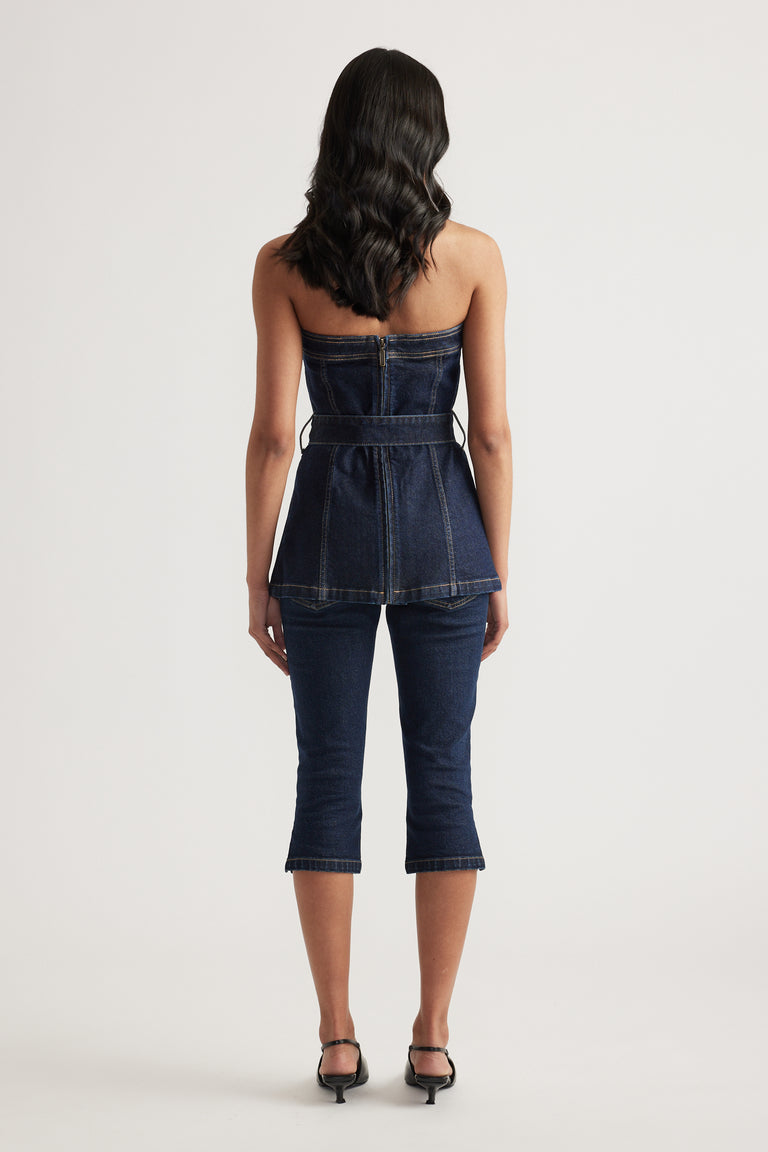 Back view of a woman wearing a strapless denim peplum top, slim capri jeans and black heels