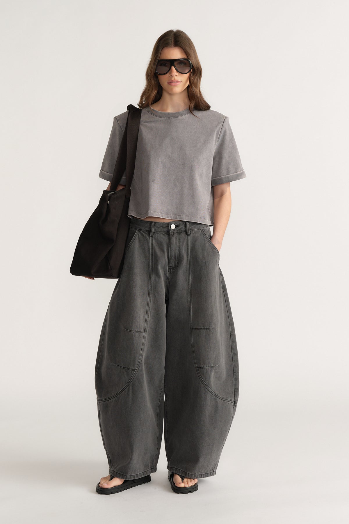 Woman wearing loose dark grey wide-leg jeans with front pockets, grey cropped t-shirt, black tote bag, and sunglasses