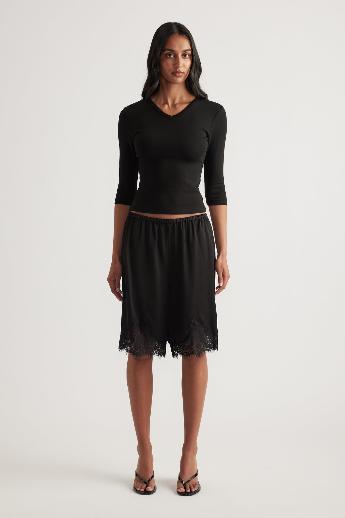Woman wearing a fitted black V neck top with three quarter sleeves and a black skirt with a lace hem