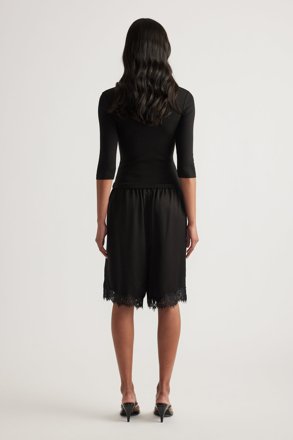 Woman viewed from behind in a black fitted three quarter sleeve top and lace trim skirt