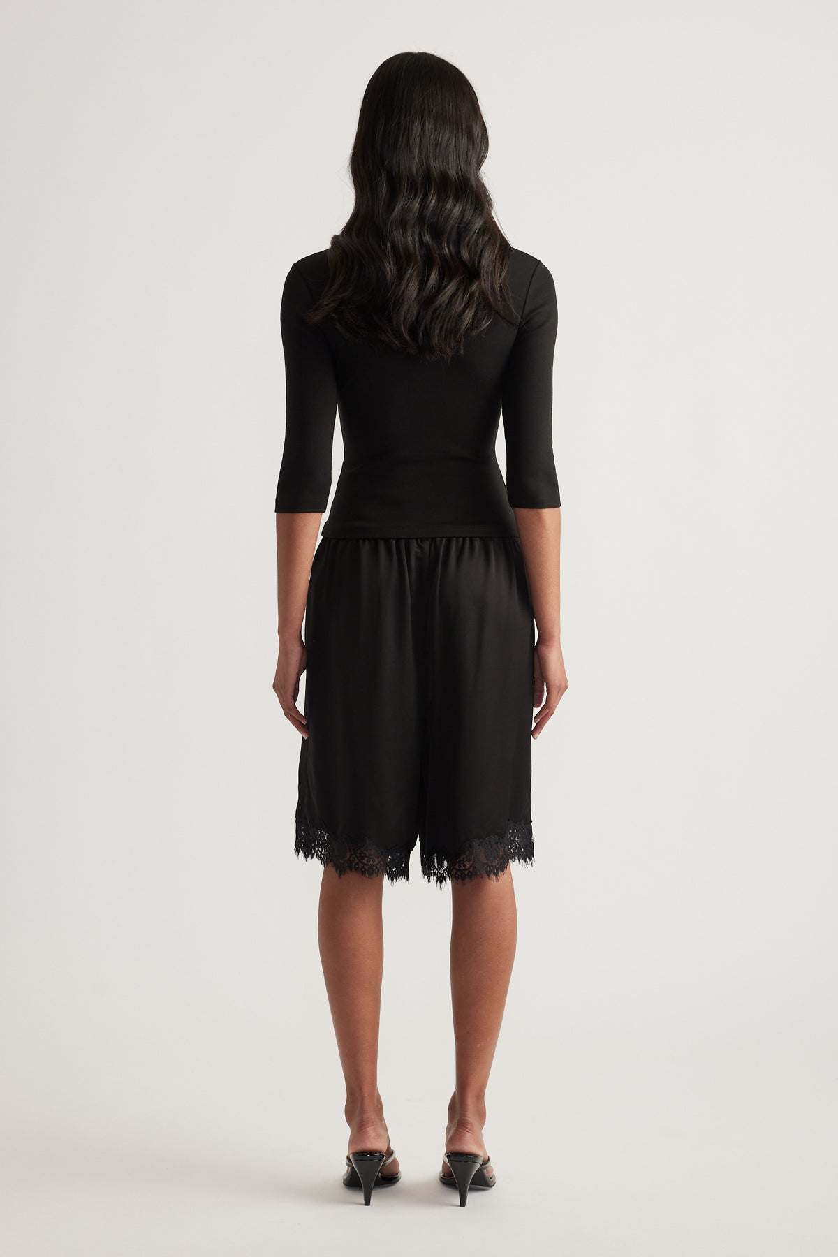 Woman viewed from behind in a black fitted three quarter sleeve top and lace trim skirt