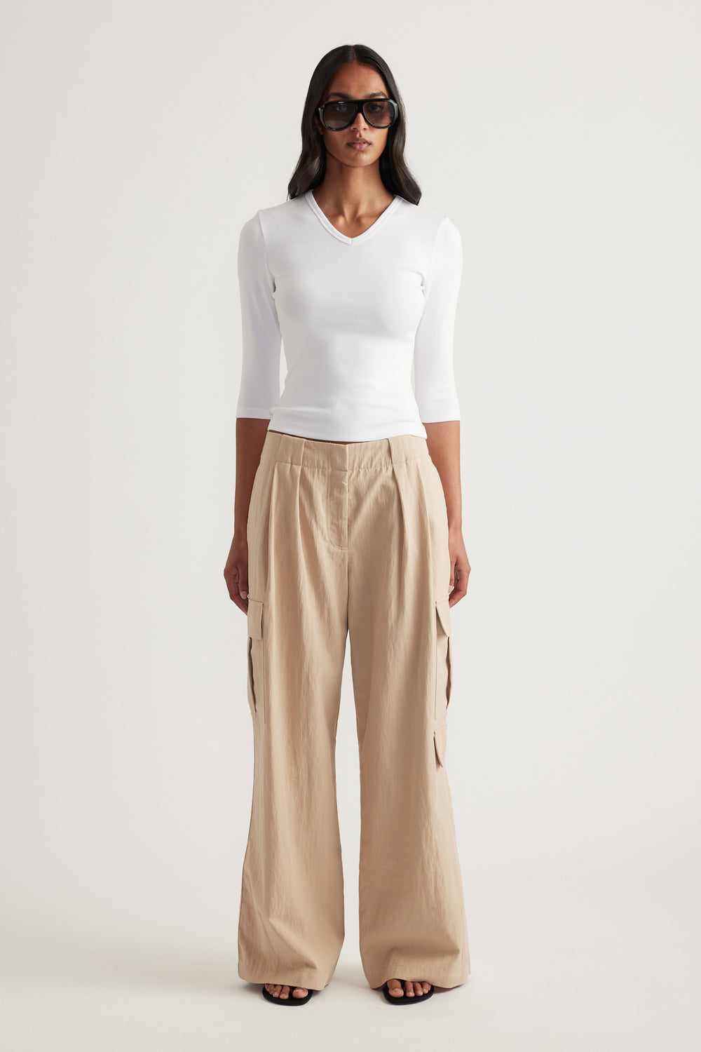 Woman wearing a fitted white V neck three quarter sleeve top with beige wide leg pants and sunglasses