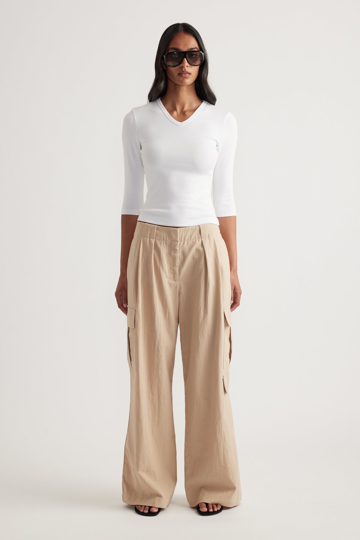 Woman wearing a fitted white V neck three quarter sleeve top with beige wide leg pants and sunglasses