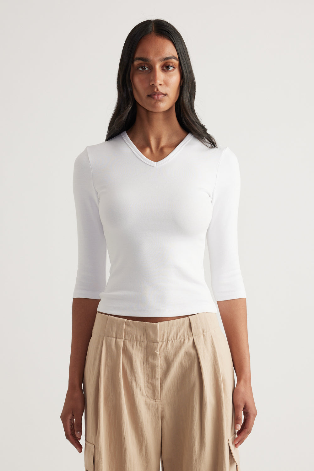 Woman wearing a fitted white V neck three quarter sleeve top with beige wide leg pants