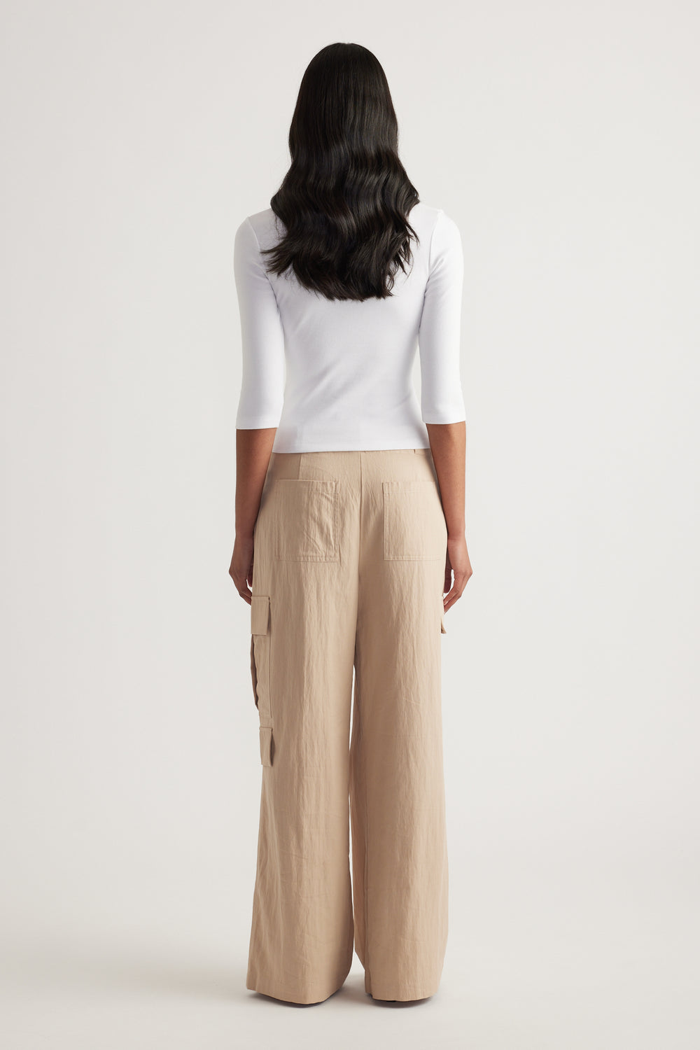 Woman viewed from behind wearing a fitted white three-quarter sleeve top and beige wide-leg pants
