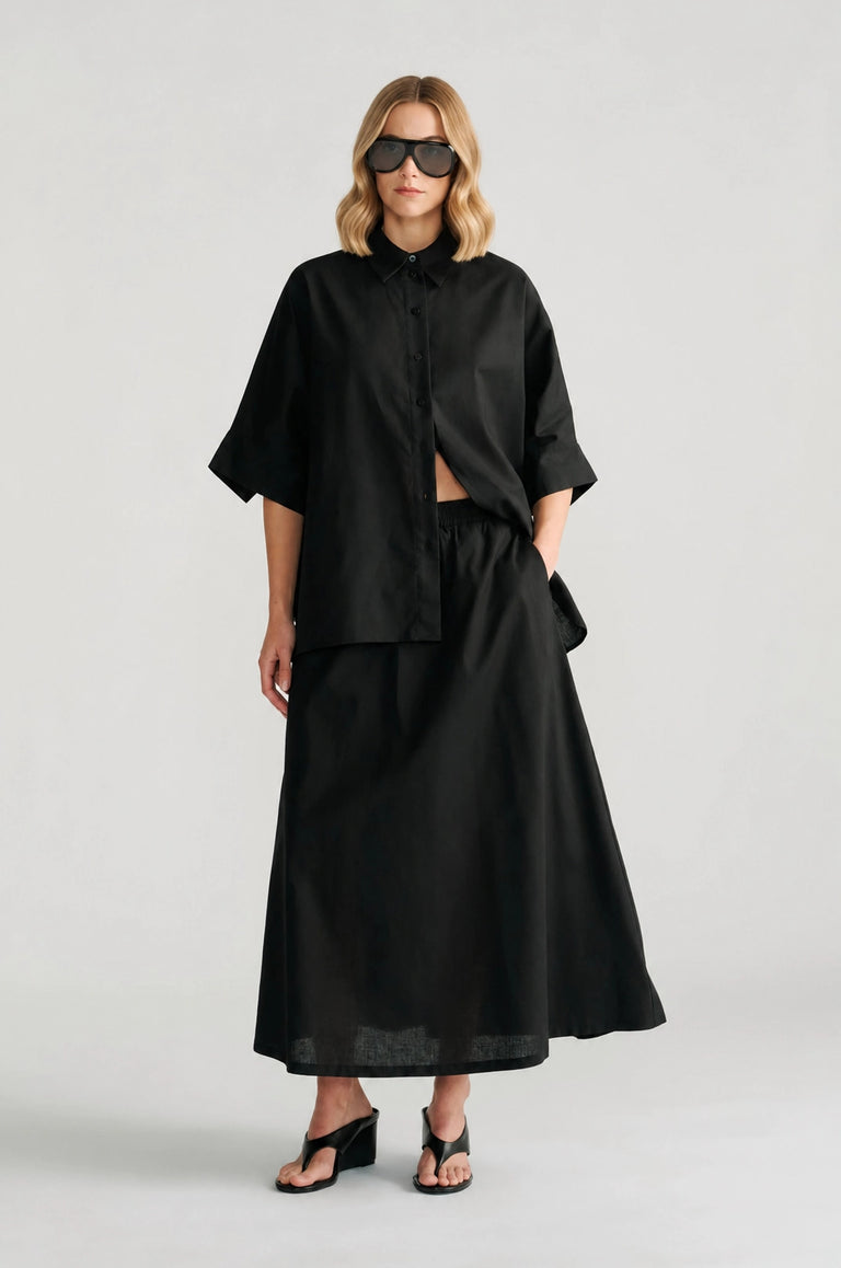 Woman wearing a relaxed black oversized shirt with elbow-length sleeves paired with a flowing black maxi skirt and heels
