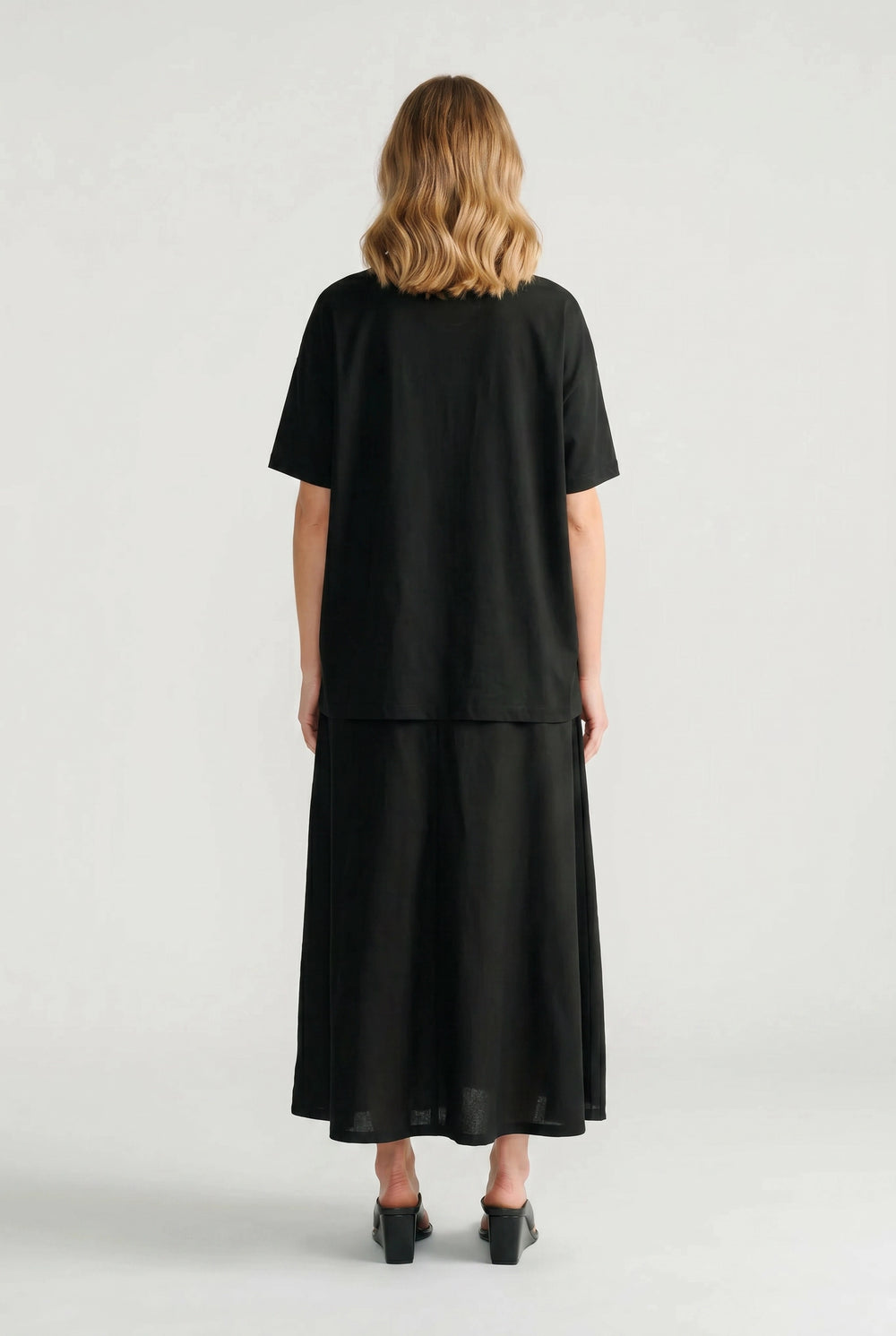 Back view of a relaxed black oversized shirt paired with a matching long skirt and black heeled sandals