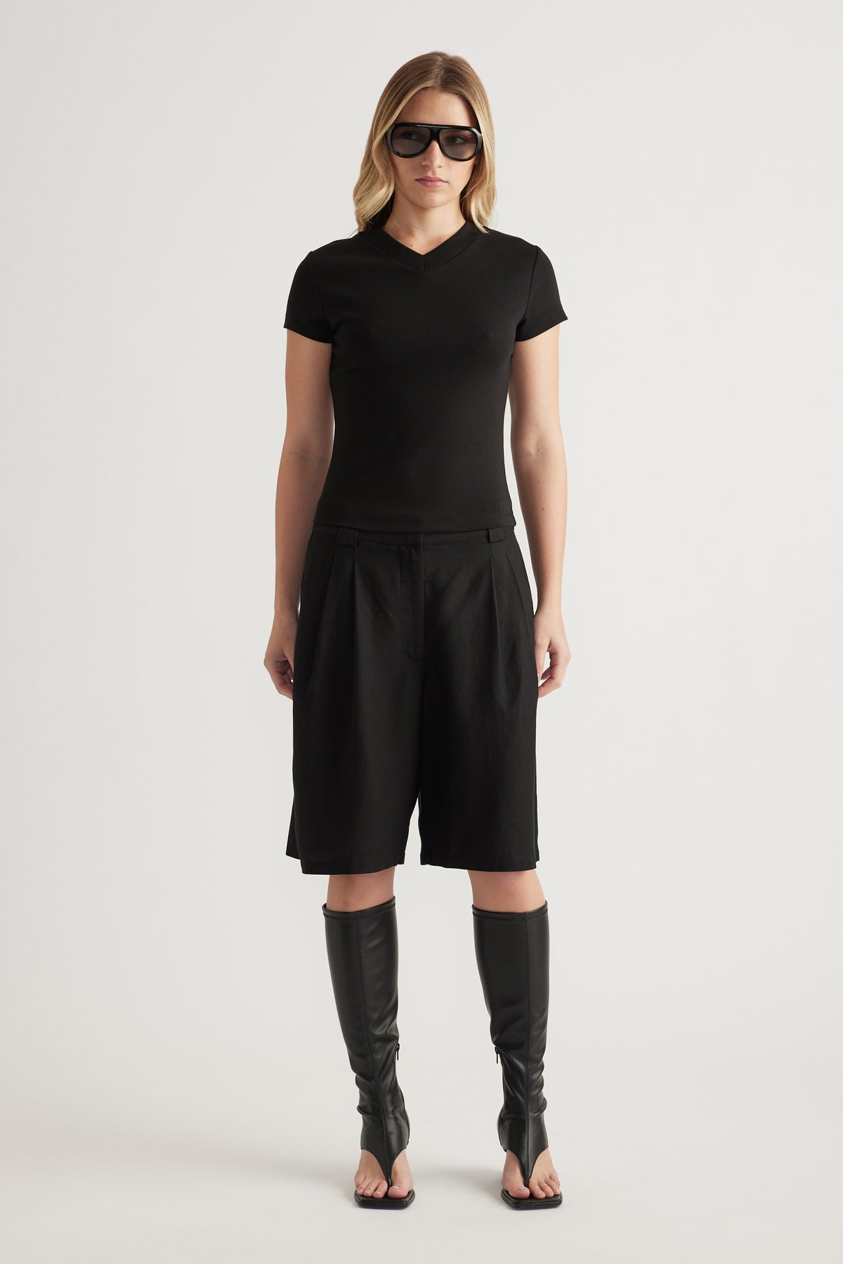 Woman wearing a black fitted V neck tee with black shorts and knee high boots