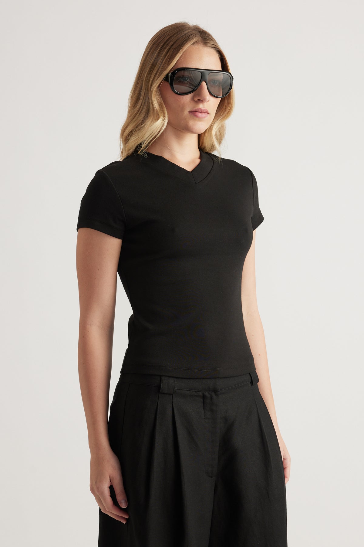 Woman in a fitted black V neck tee with short sleeves and pleated black trousers