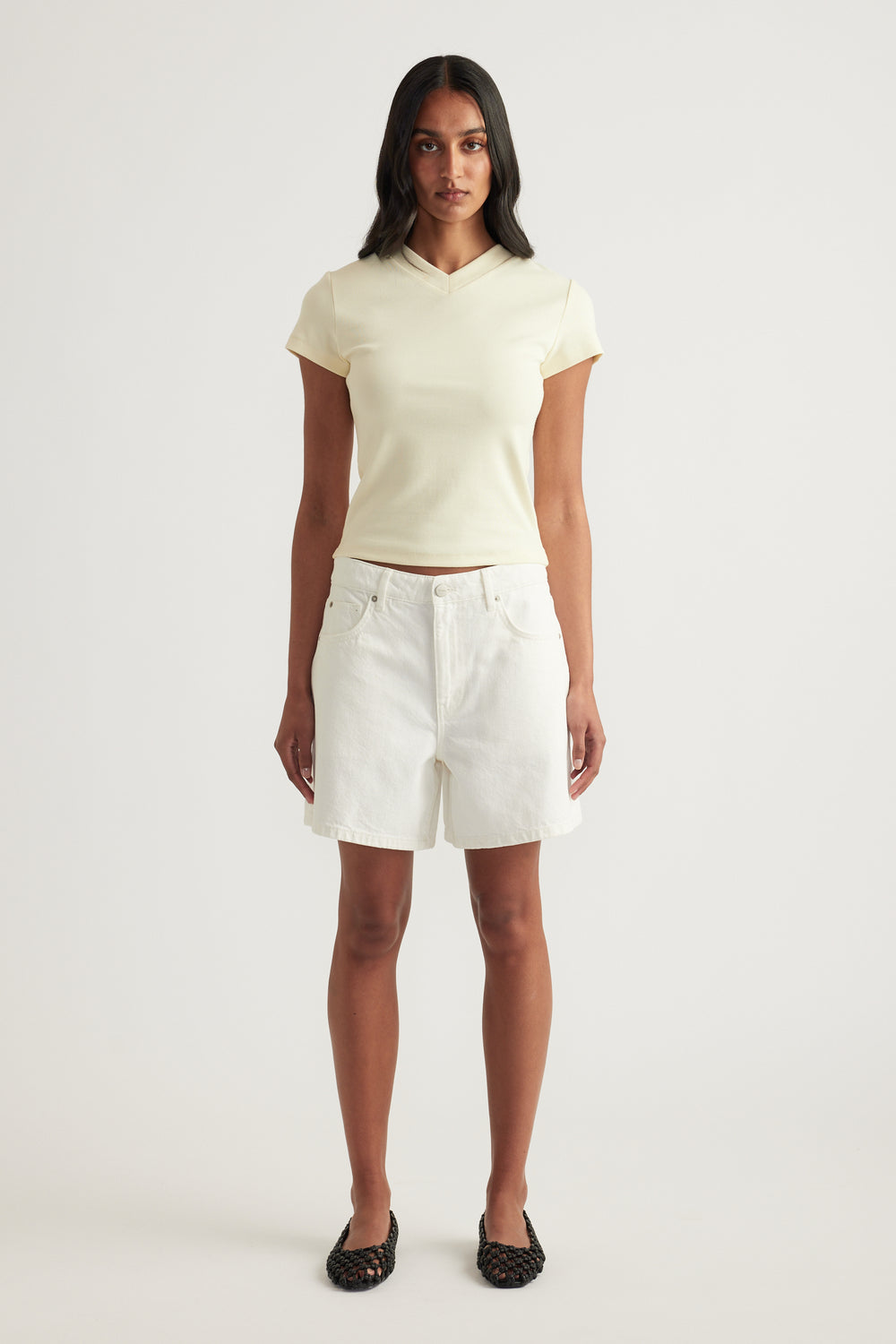 Woman wearing a cream fitted V-neck tee with white denim shorts and black flats