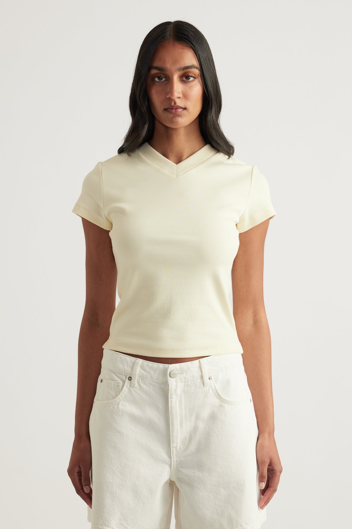 Woman wearing a cream fitted V neck tee with short sleeves and white jeans