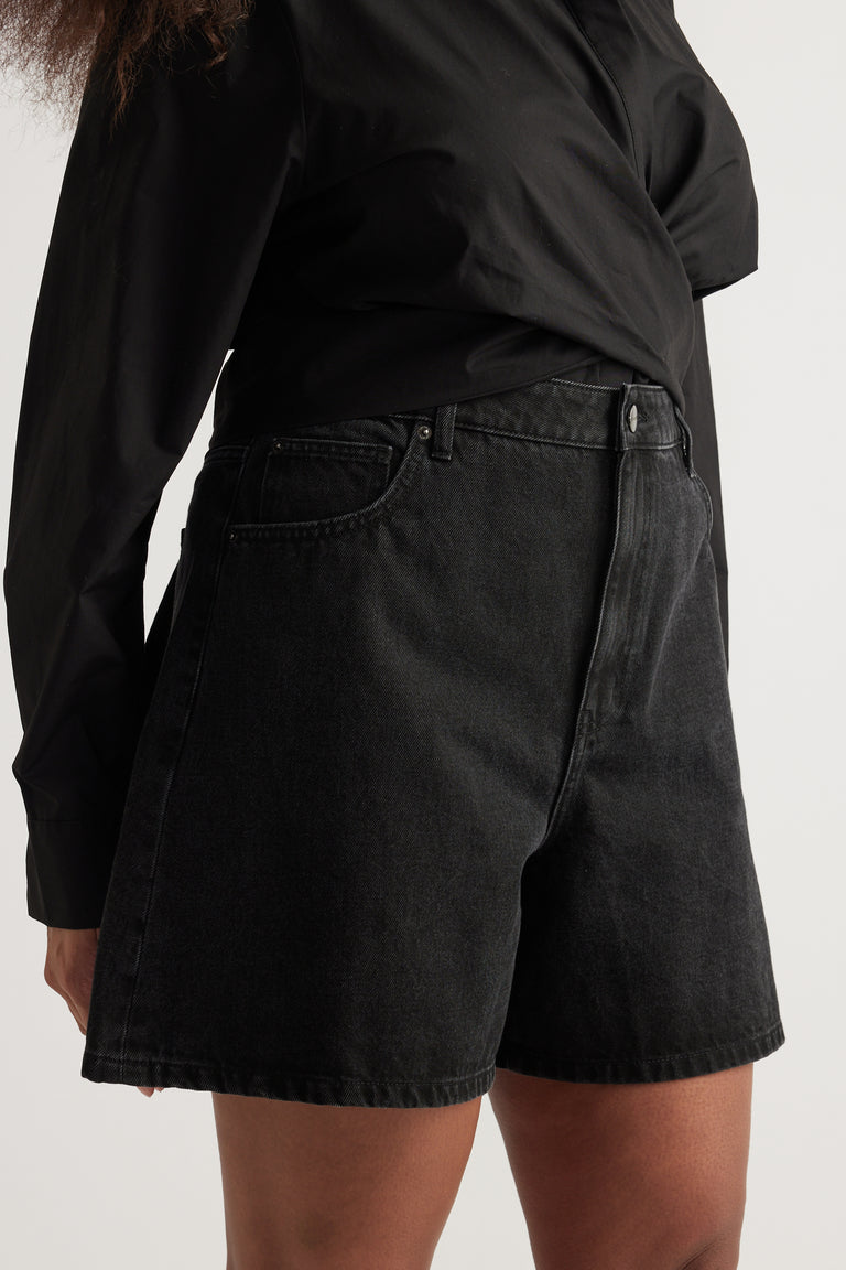 Woman wearing black high-rise A-line denim shorts with a mid-thigh length and button fly