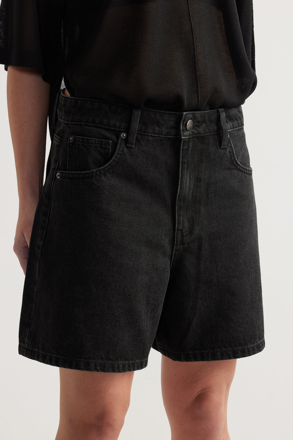 Woman wearing black high rise A line denim shorts with a black top