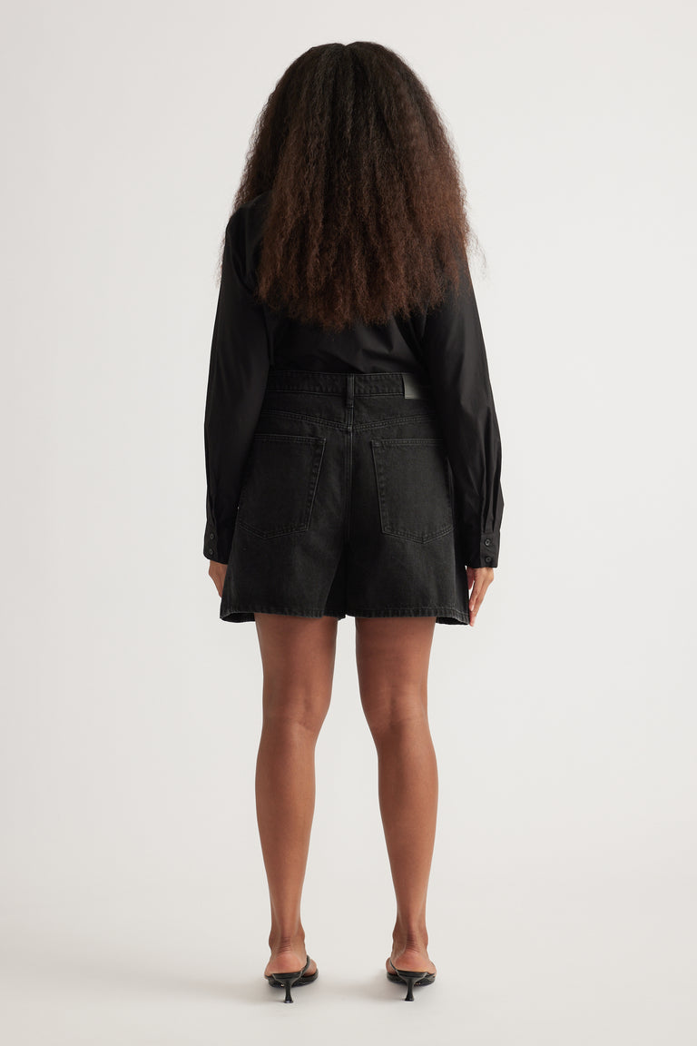 Back view of a woman wearing black denim A-line shorts with a black long-sleeve blouse