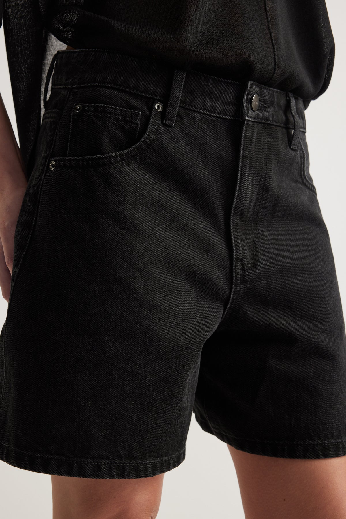 Close-up of woman wearing black high-rise A-line denim shorts with five-pocket styling